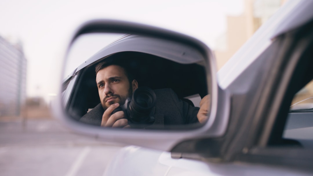 Young private detective man sitting inside car and photographing with slr camera